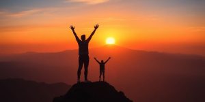 Person celebrating atop a mountain during a sunrise.