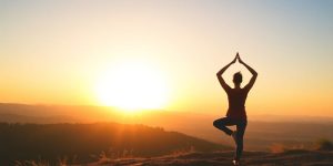 A person practicing yoga at sunrise in a peaceful landscape.